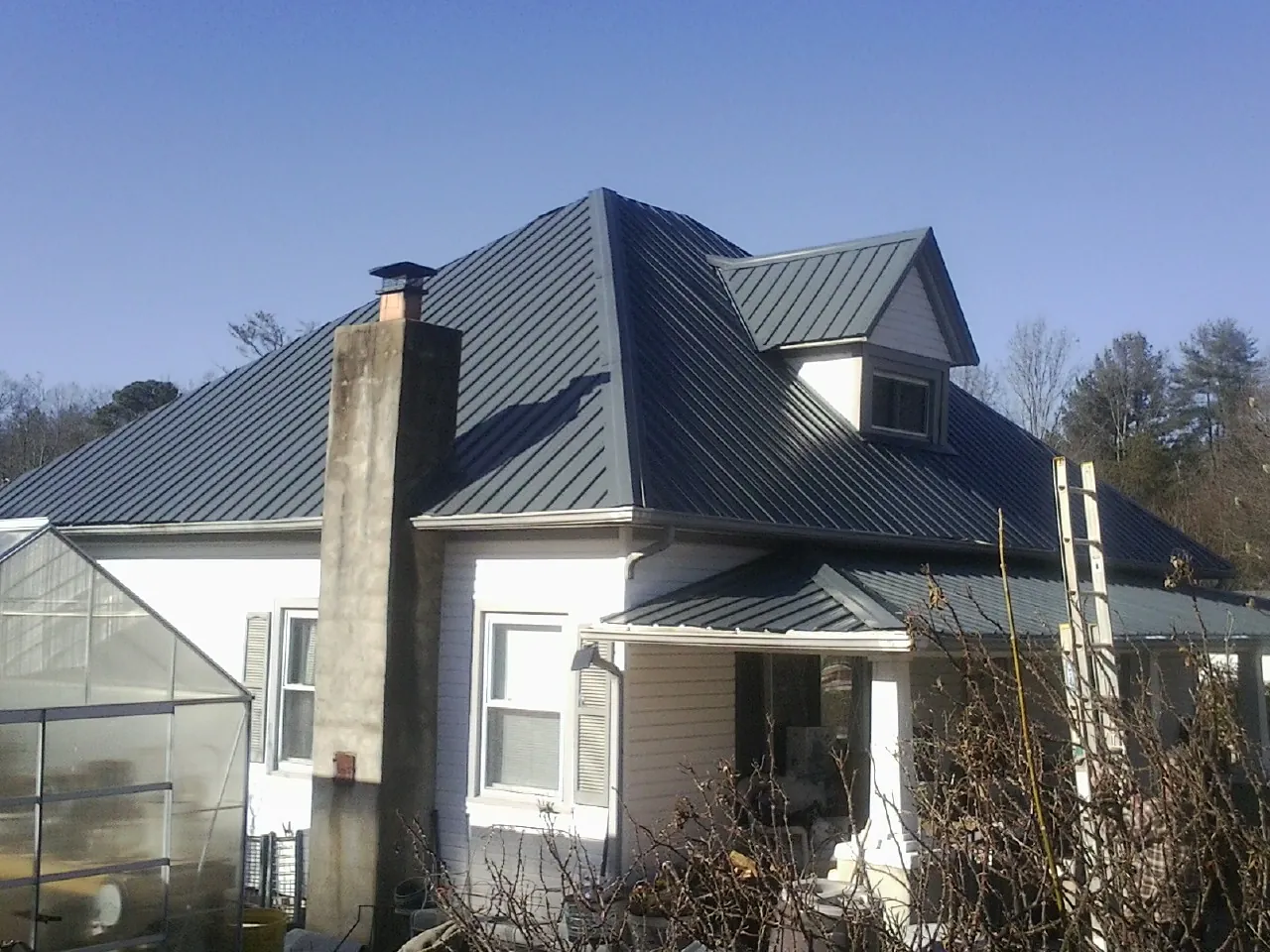 Dark blue standing seam metal roof on a white farmhouse with dormer — Slate & Tile Roof Repair by Roofing Brothers in Abilene