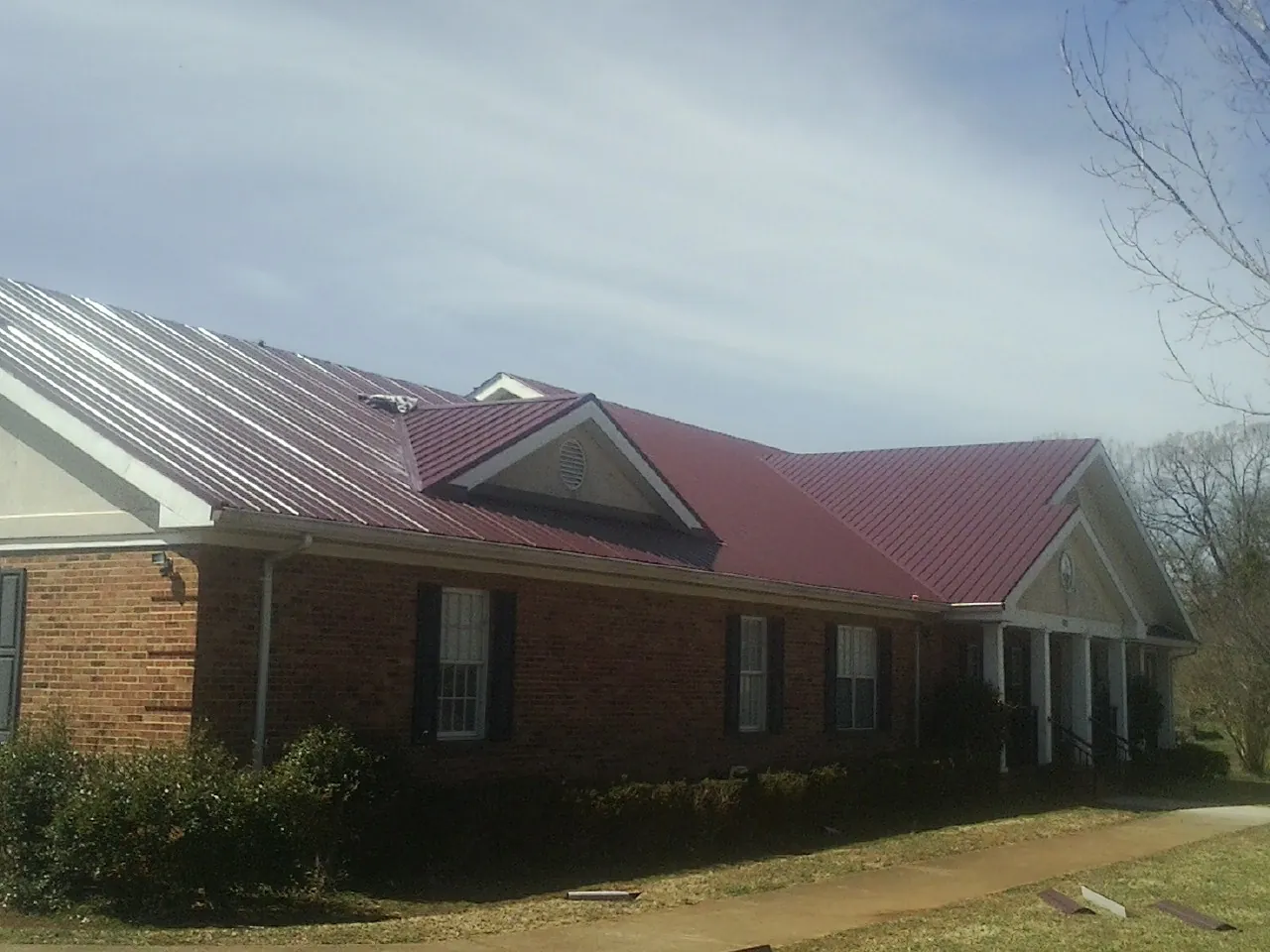Red metal roof with gabled entries on a long brick building, from a Hail Damage Roof Repair job in Abilene