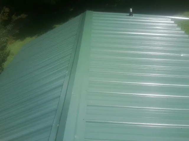New green metal panels meeting at the ridge of a roof — Flat Roof Repair work by our crew in Abilene